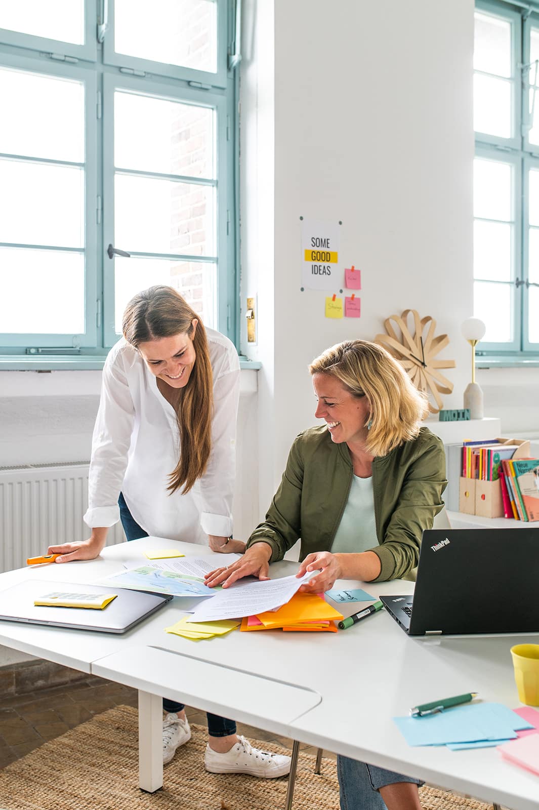 Mitarbeiterinnen bei der Zusammenarbeit im Büro, kreative Arbeitsumgebung, Dokumente und Laptop auf.