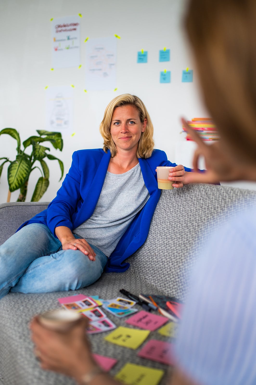 Frau im blauen Blazer bei einem Team-Meeting im Büro, Notizen und Post-its auf dem Tisch.