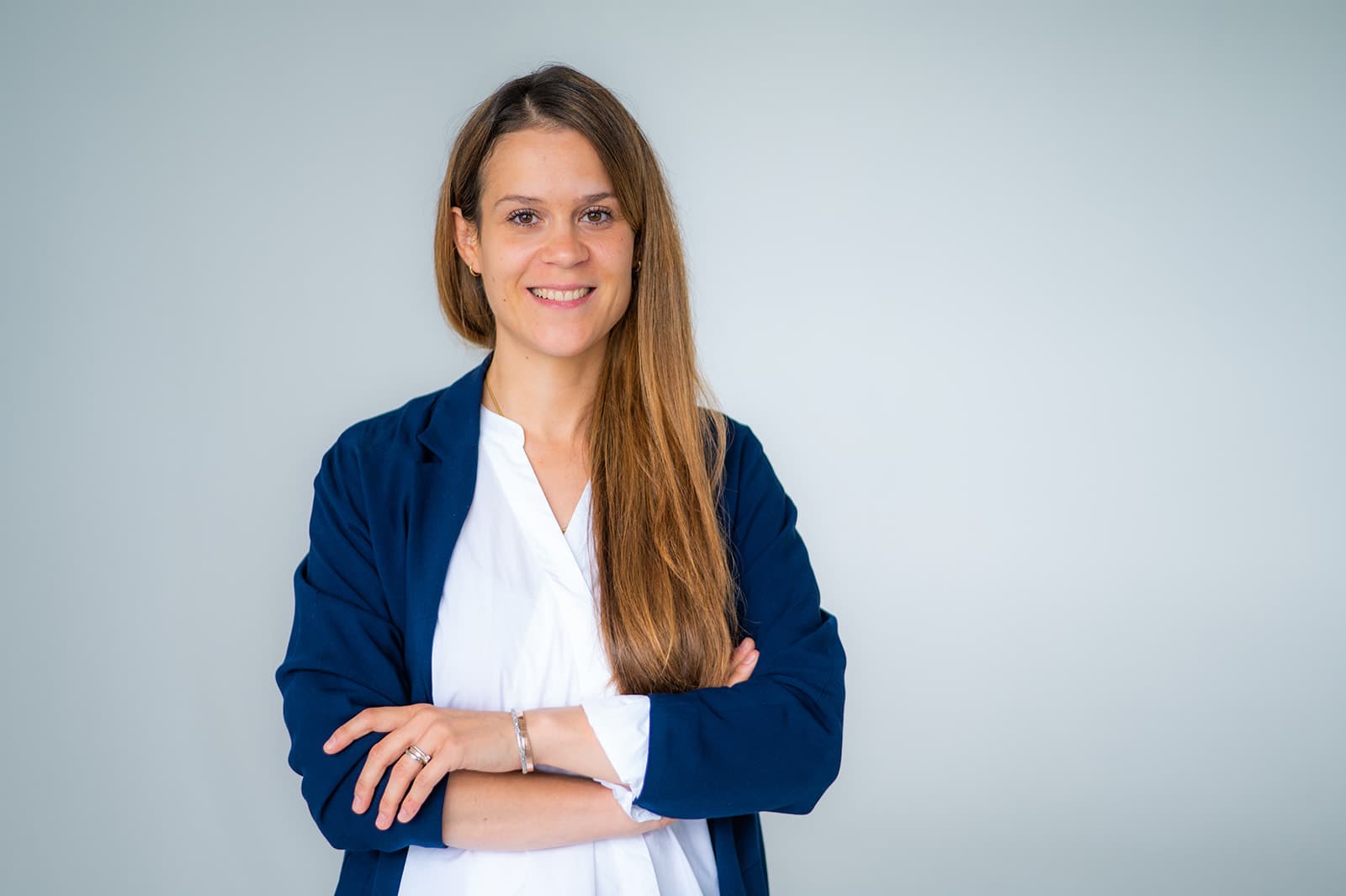 Frau im Business-Outfit vor neutralem Hintergrund, professionell und freundlich.