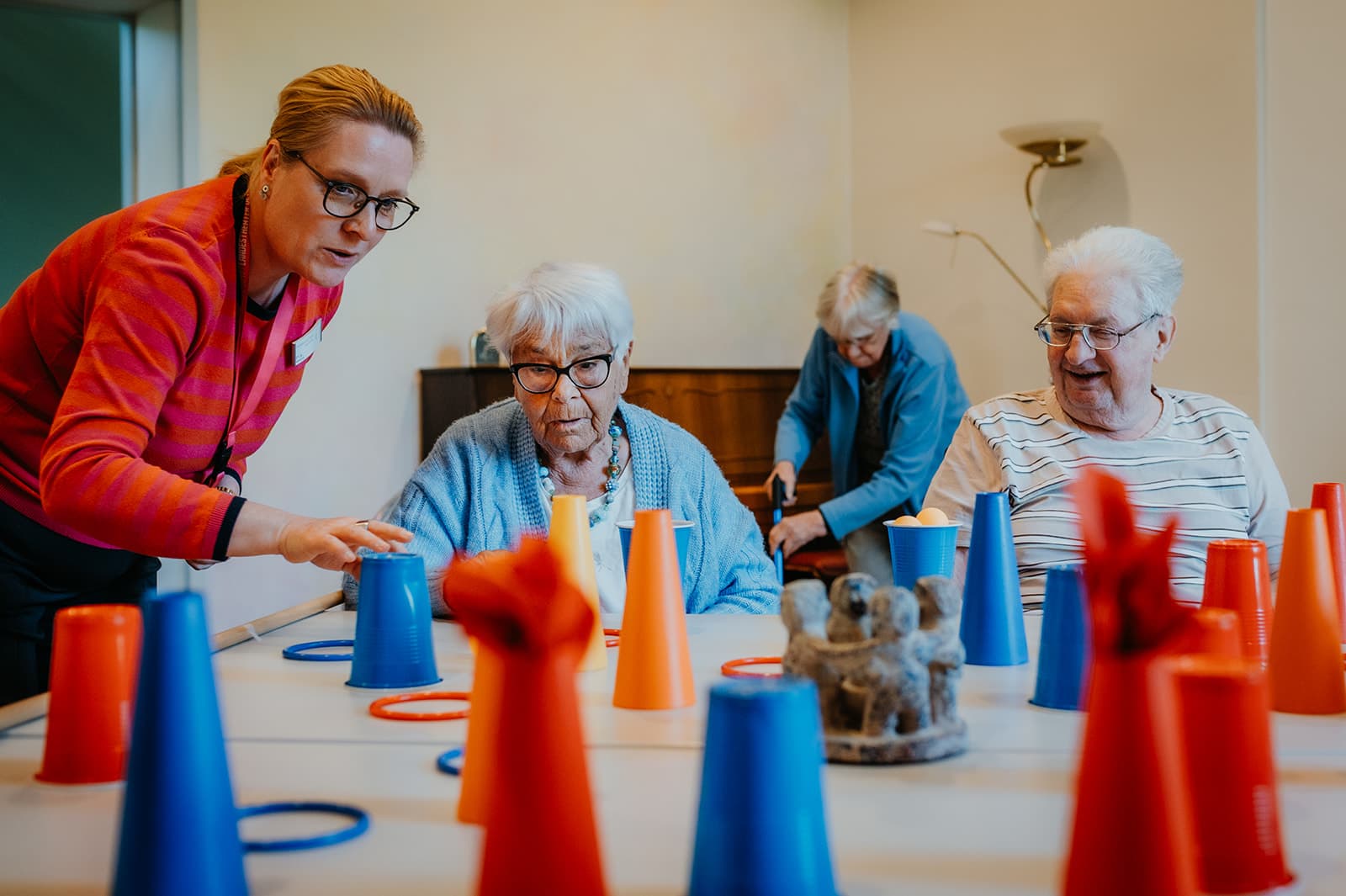 Personal Branding Fotografie im Christophorus Pflege Havelhöhe Seniorenheim – Senior*innen spielen mit Bechern und Ringen am Tisch, begleitet von Betreuungsperson