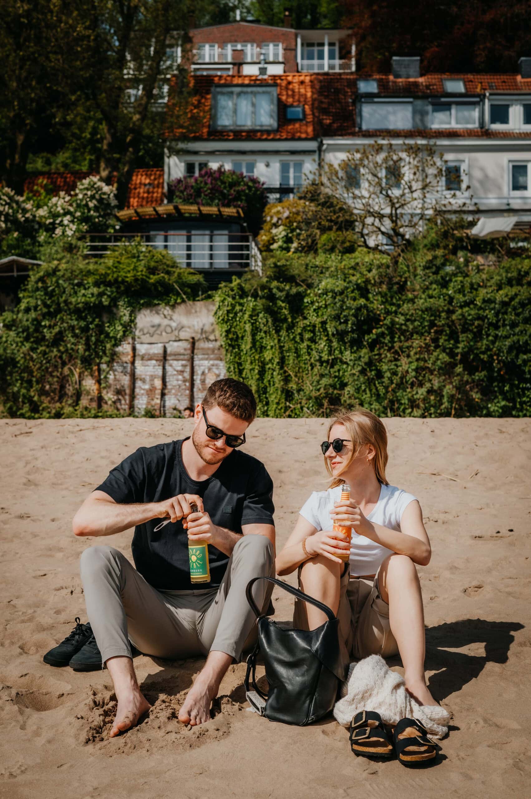 Paar sitzt am Elbstrand und öffnet zwei Flaschen Apfelsaft