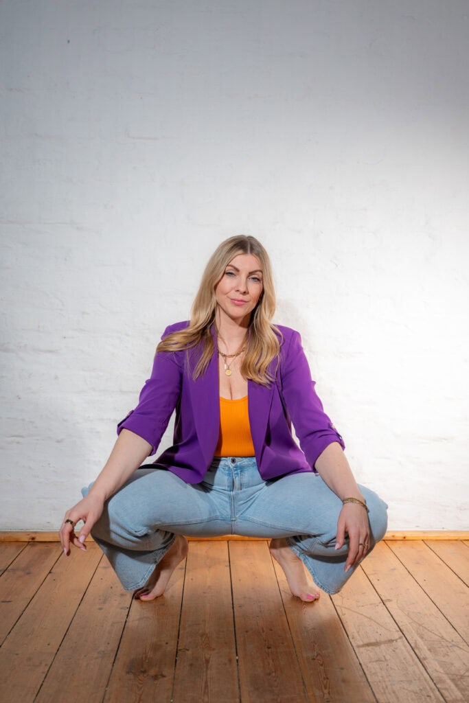 Frau in bunter Kleidung in Yoga-Pose auf Holzfußboden, entspannt und selbstbewusst.