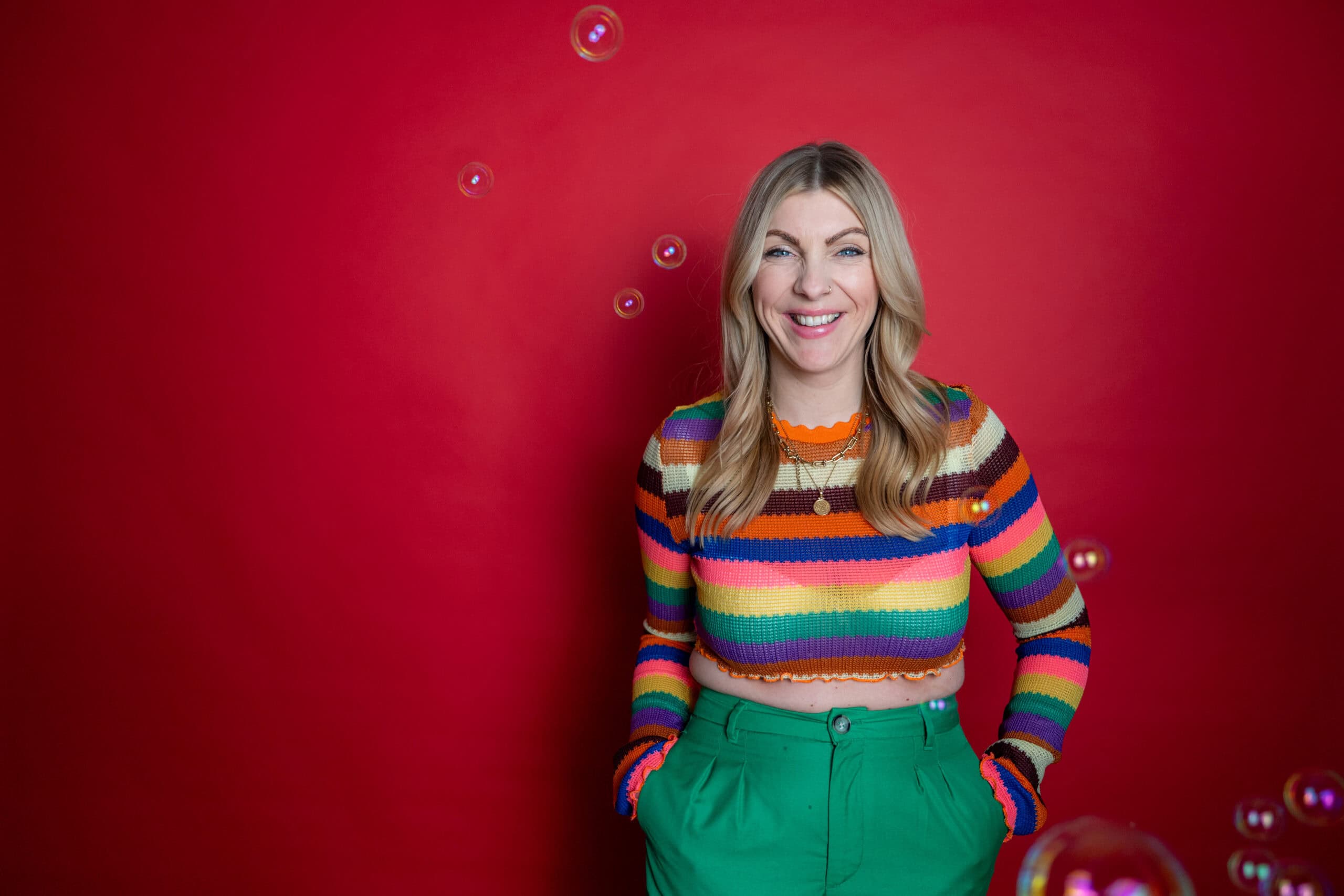 Glückliche Frau in buntem Pullover vor rotem Hintergrund, lachend und fröhlich.