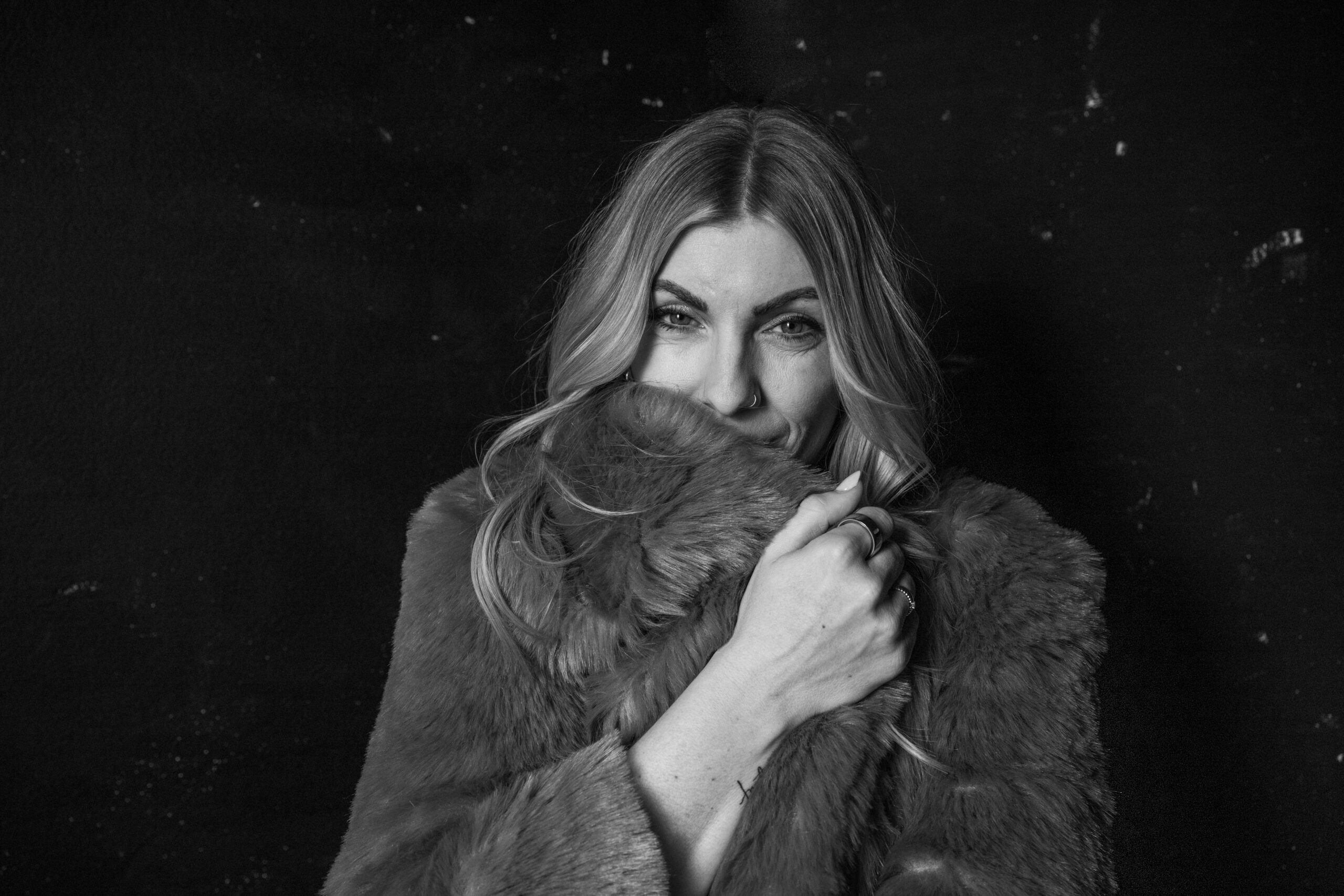 Frau mit Fellmantel, lächelnd, in Schwarz-Weiß, stilvoll und elegant.