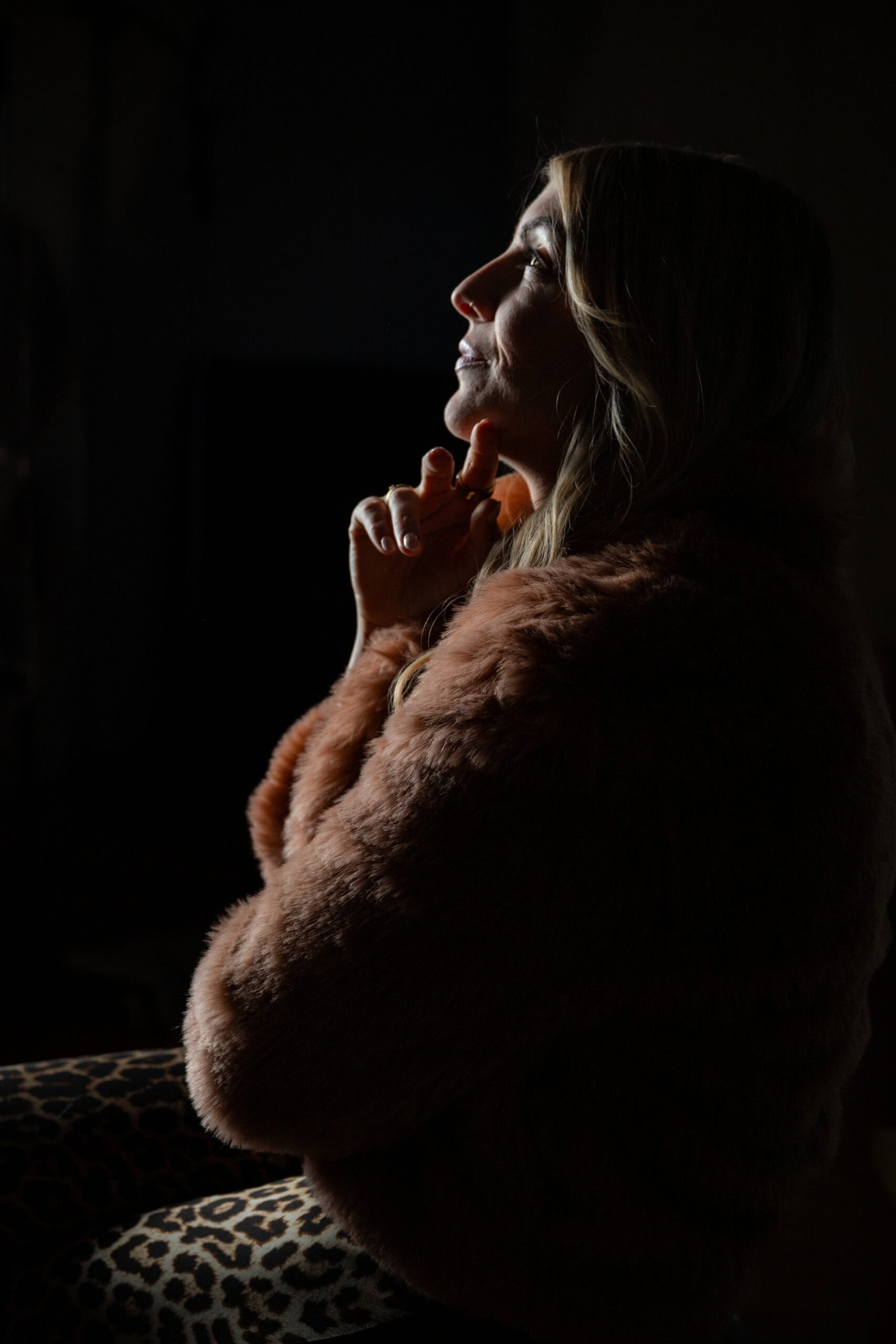 Nachdenkliche Frau in Fuchspelzjacke, im Schatten, ruhiger Moment.