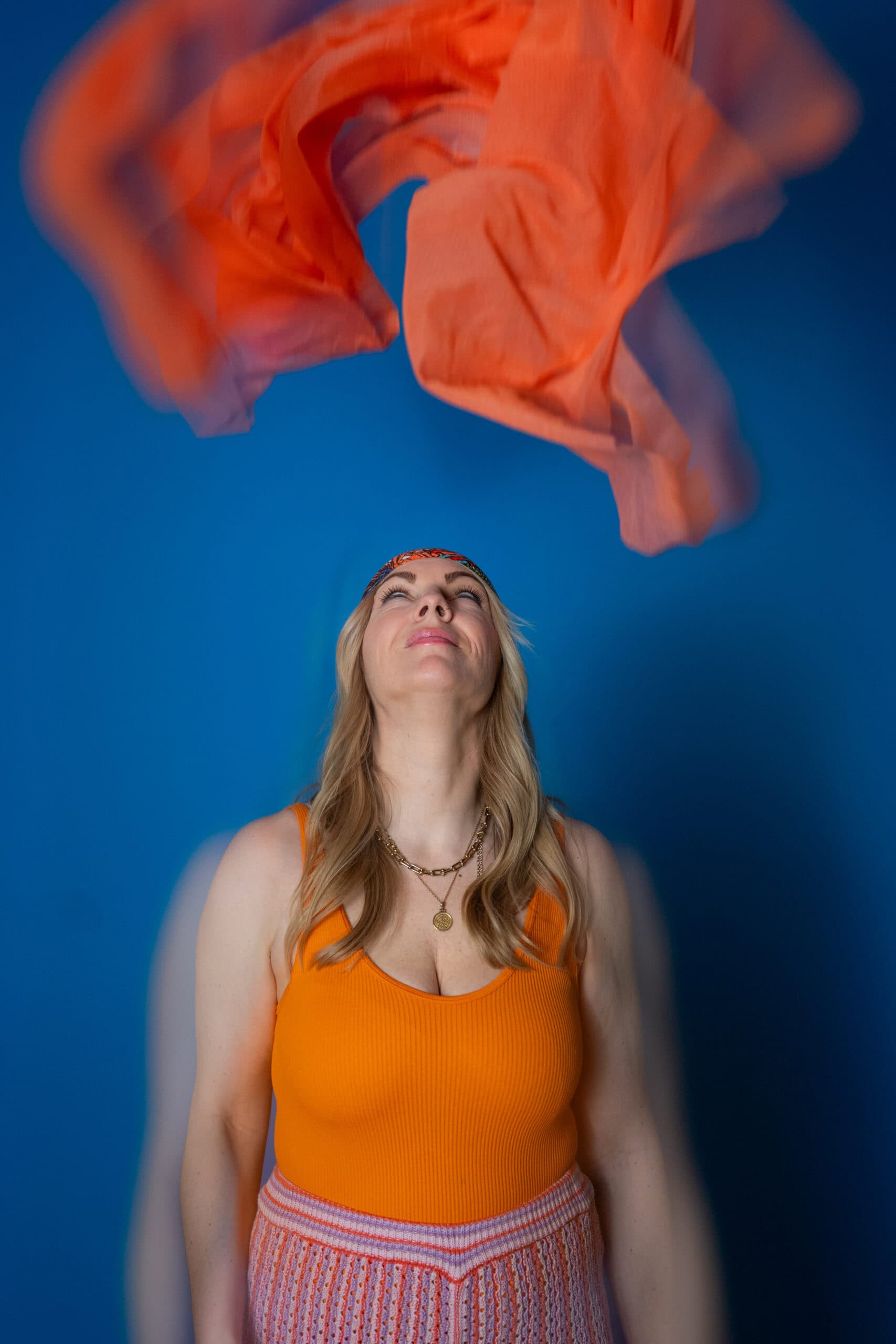 Frau wirbelt bunte Tücher in der Luft vor einem blauen Hintergrund.