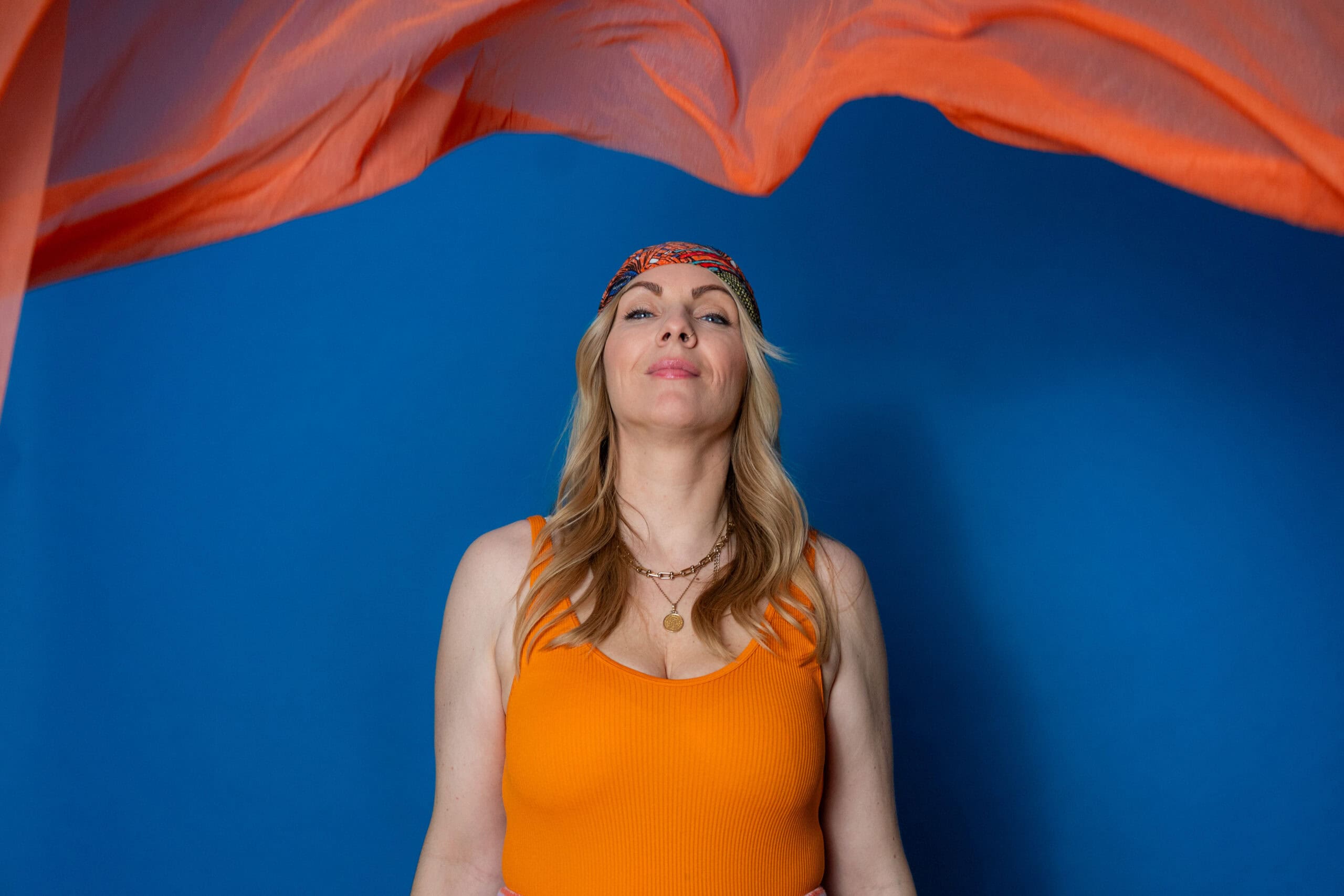 Frau entspannt unter einem orangefarbenen Tuch, mit blauer Wand im Hintergrund, symbolisiert Kreativ.