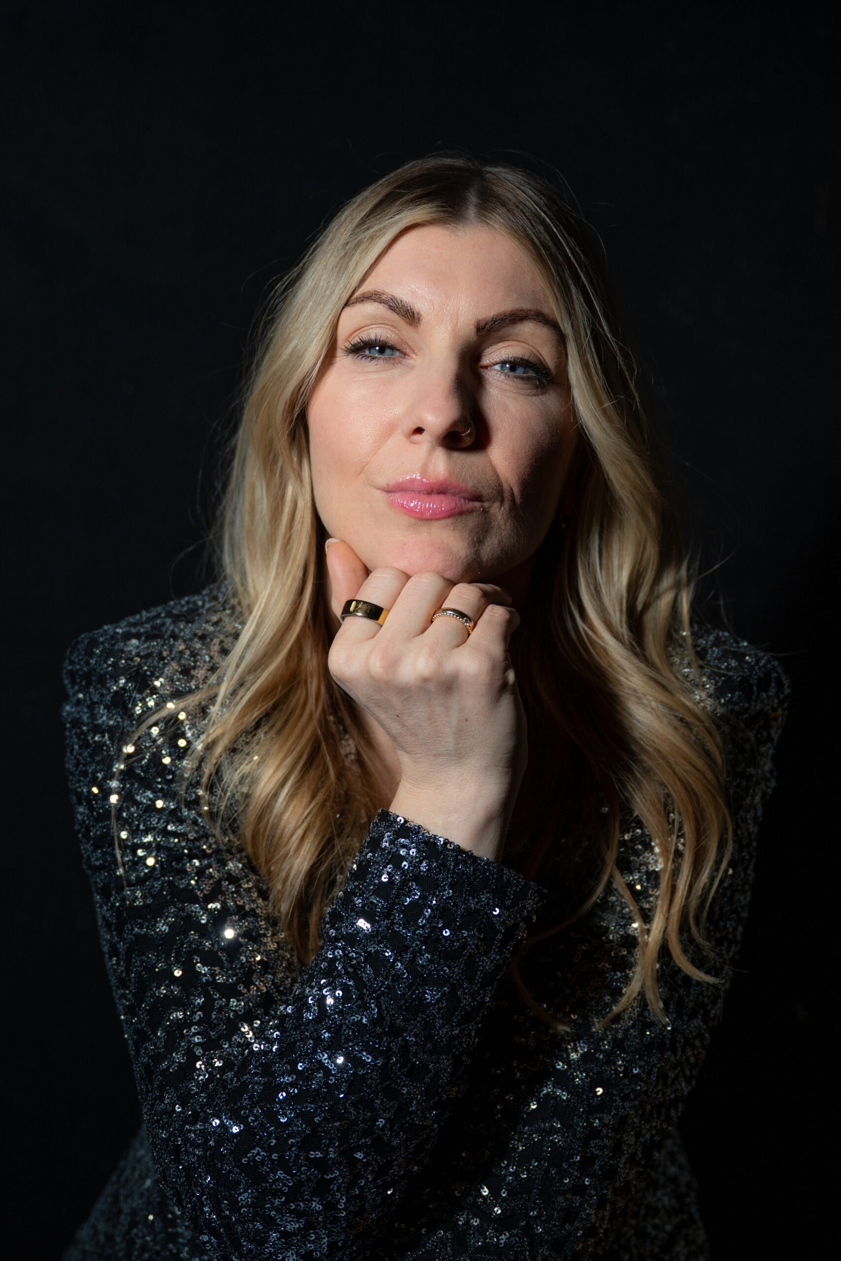 Selbstbewusste Frau in Paillettenkleid, nachdenklich, auf dunklem Hintergrund.