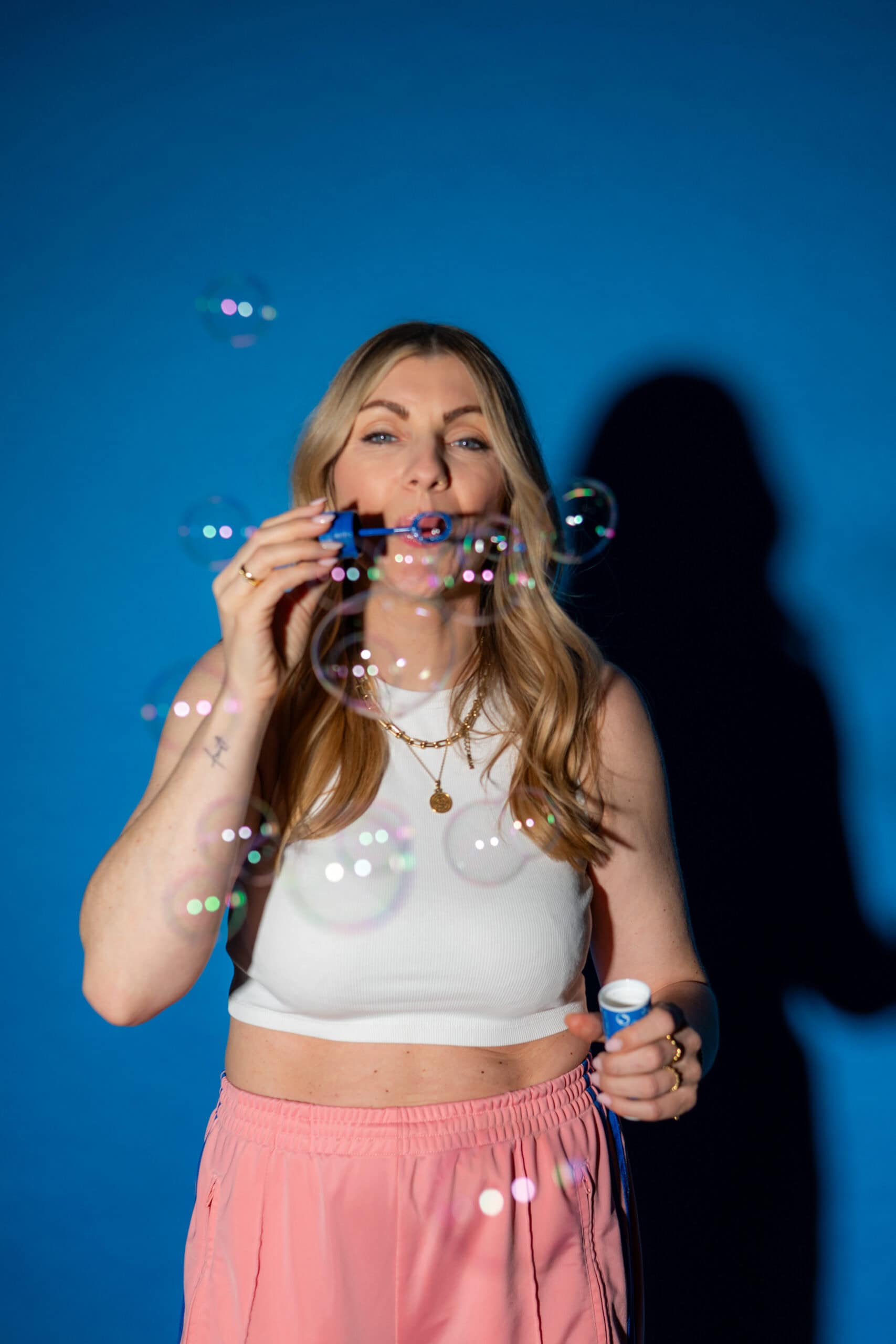 Frau macht Seifenblasen vor blauem Hintergrund, kreative Freizeitaktivität.