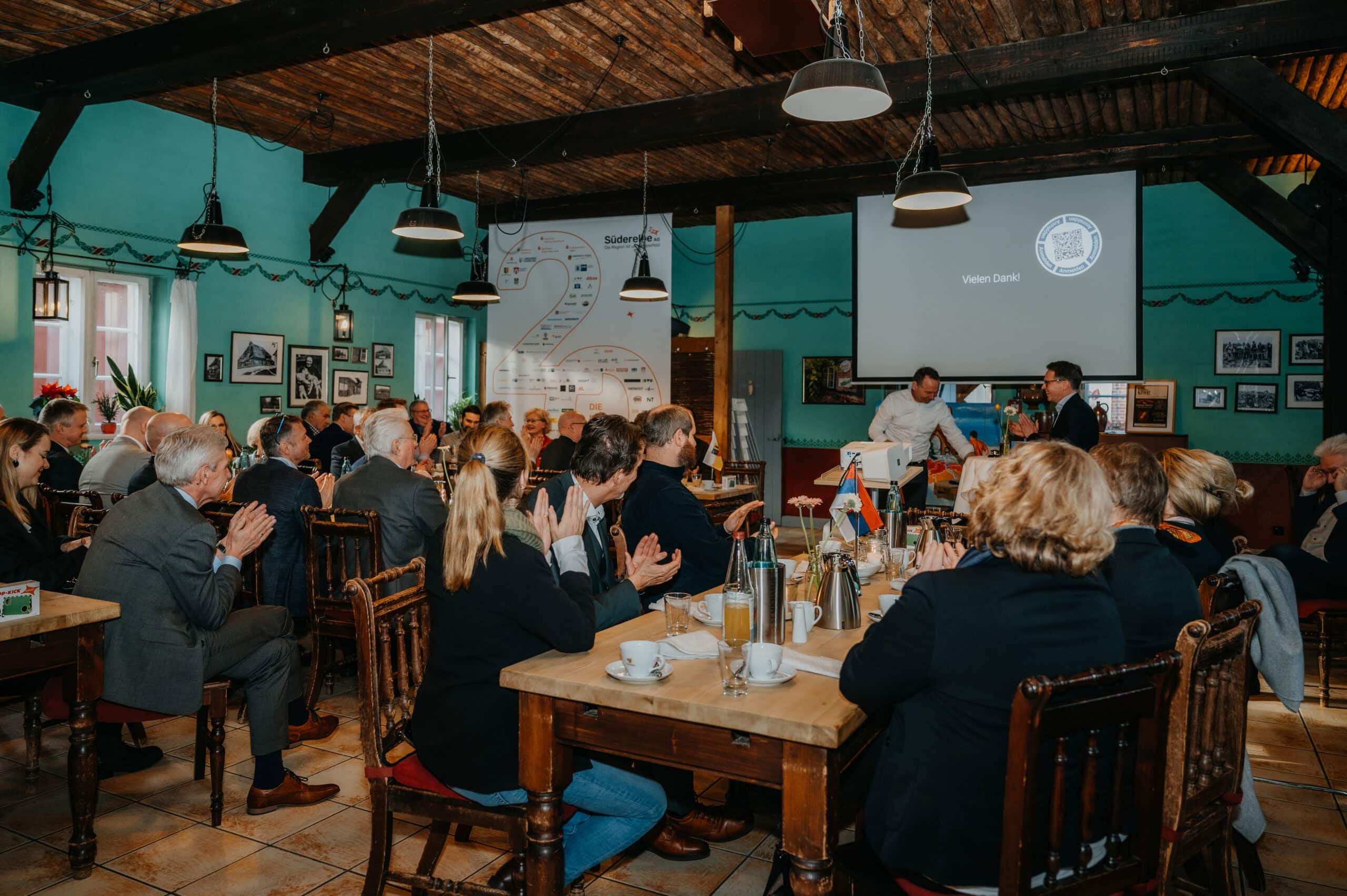 Geschäftstreffen mit mehreren Teilnehmern in einem rustikalen Lokal, Präsentation auf Leinwand im Hi.