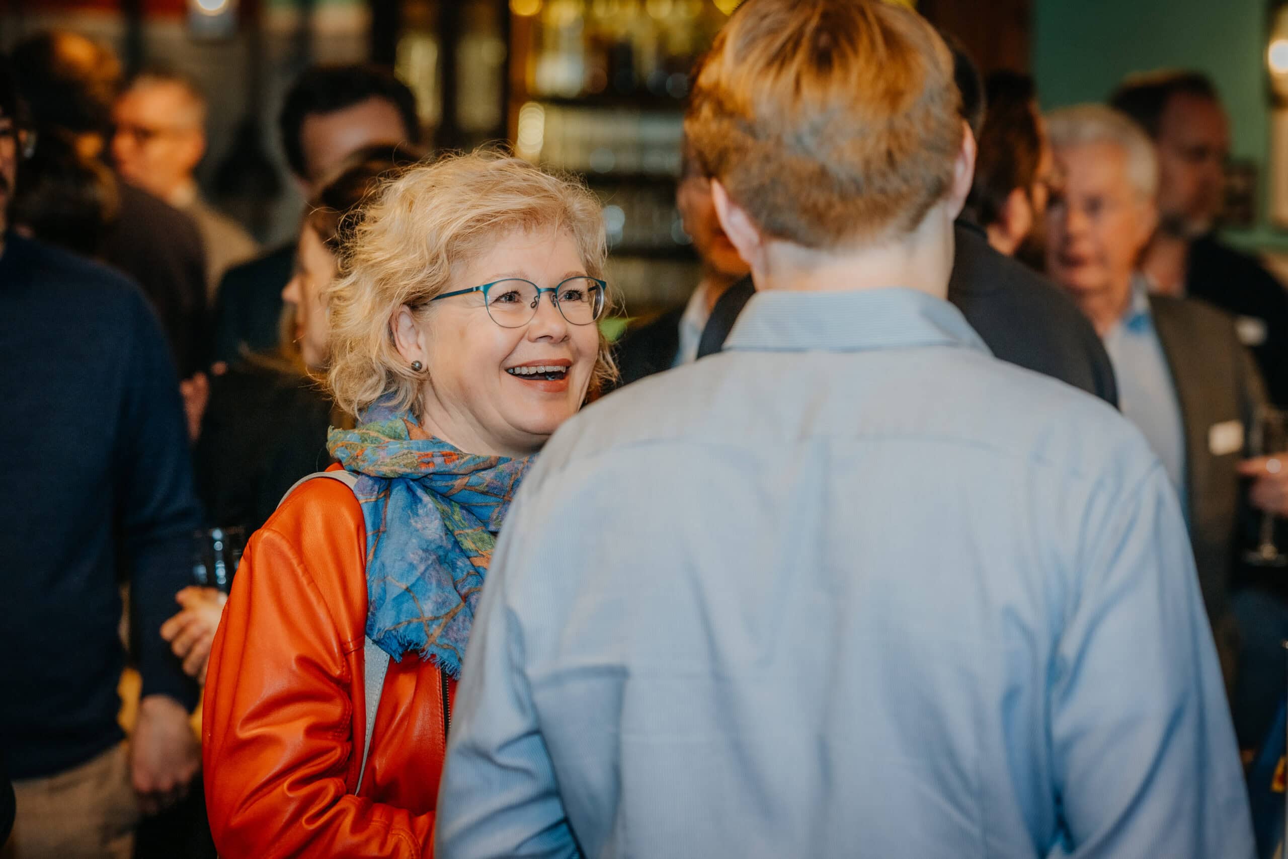 Frau im Gespräch mit einem Mann bei einer Veranstaltung, lachend und freundlich.