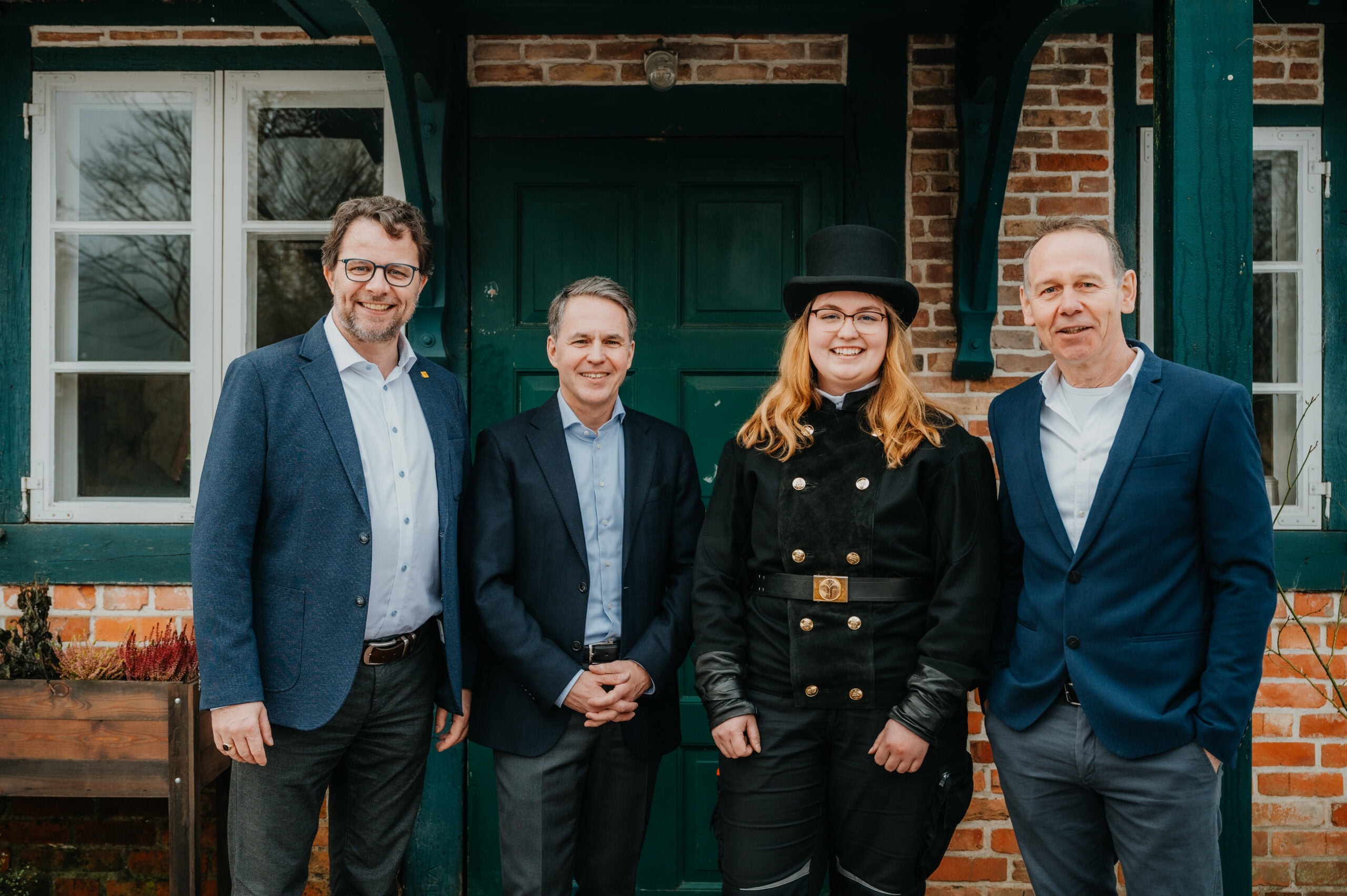 Gruppe von vier Personen vor einem grünen Tür mit Backsteinmauer.