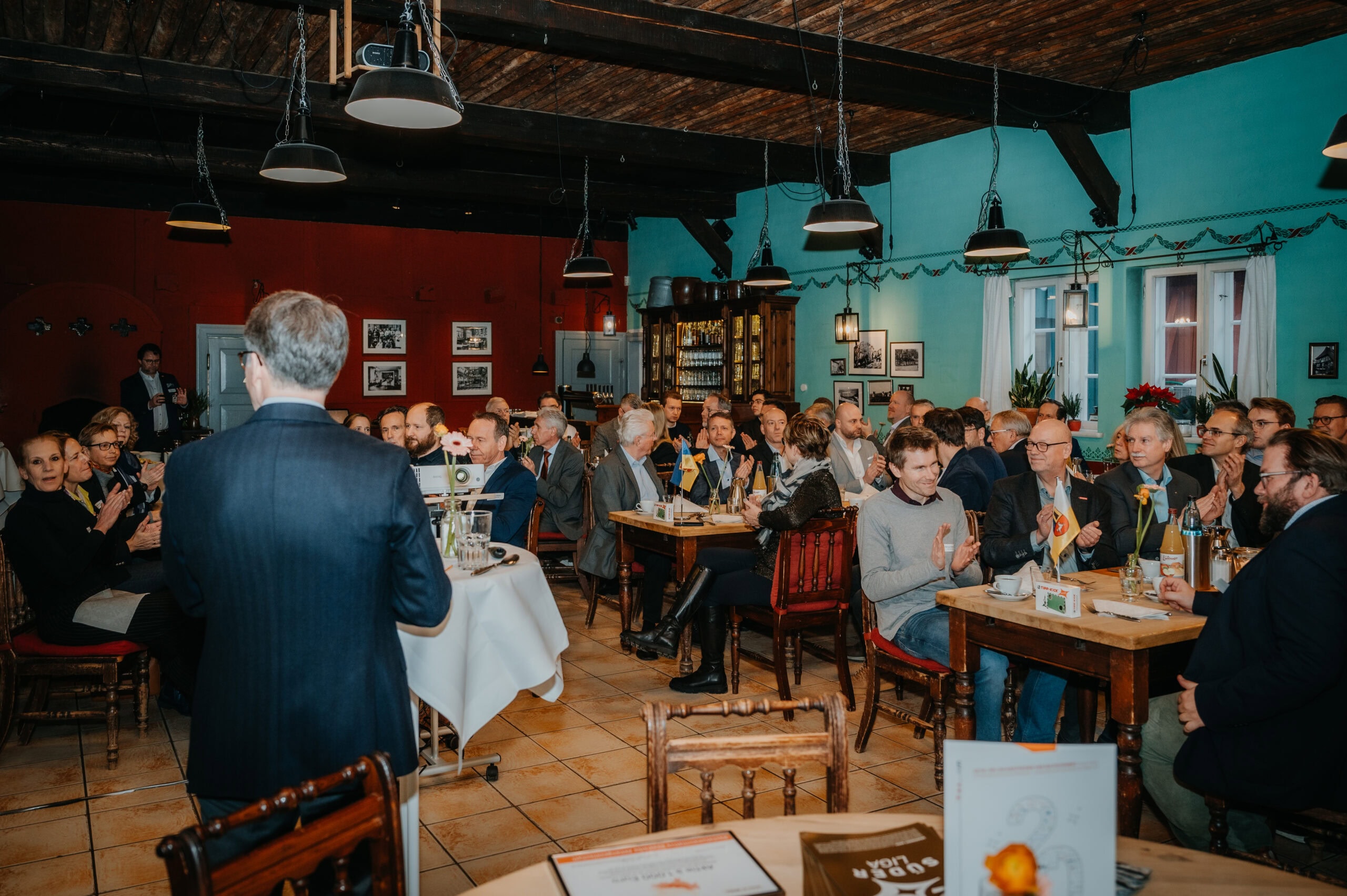 Veranstaltung im Restaurant mit vielen Gästen, Redner und gemütlicher Atmosphäre.
