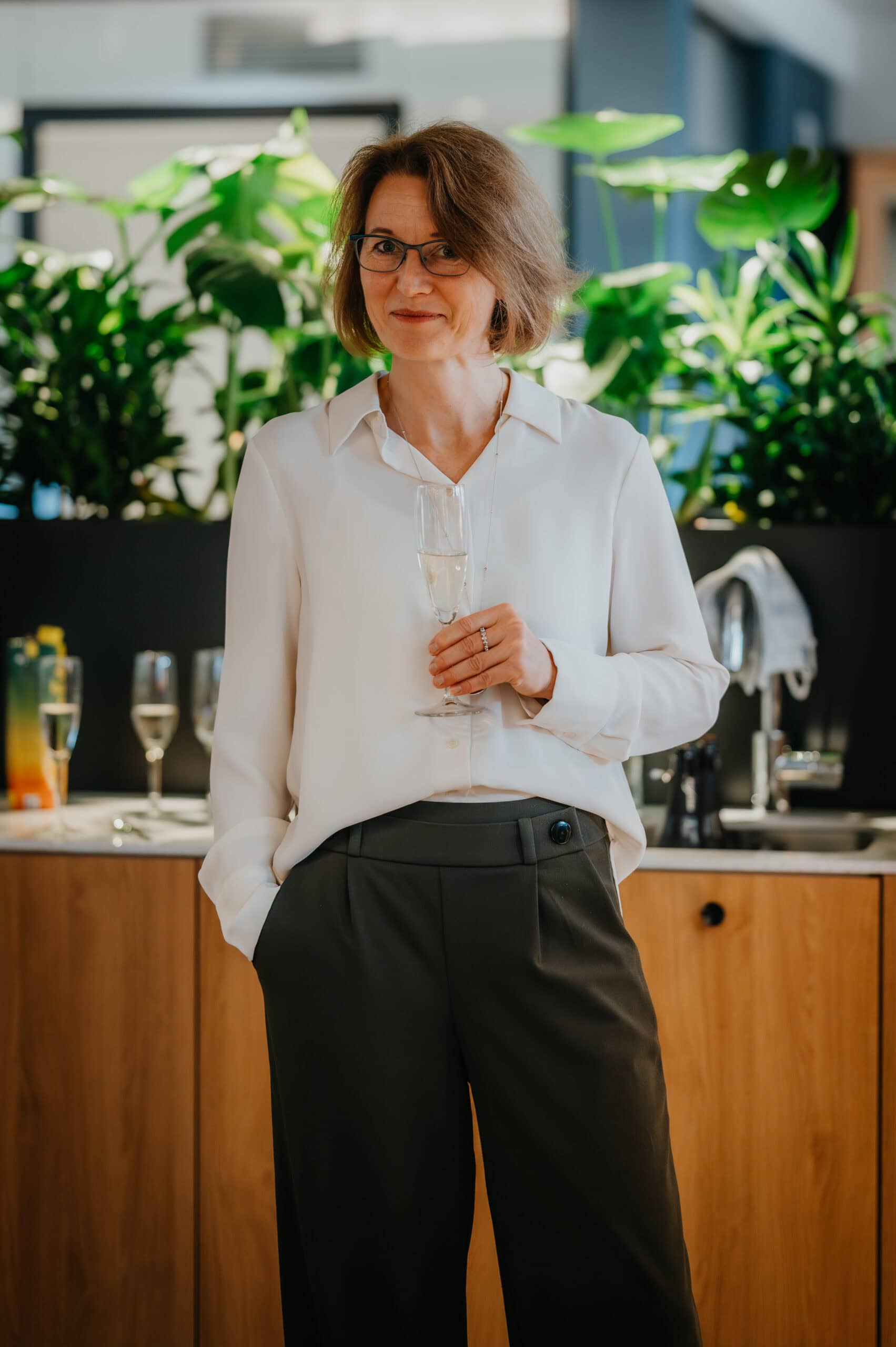 Frau bei Vertelln-Event in stilvollem Raum mit Pflanzen im Hintergrund.