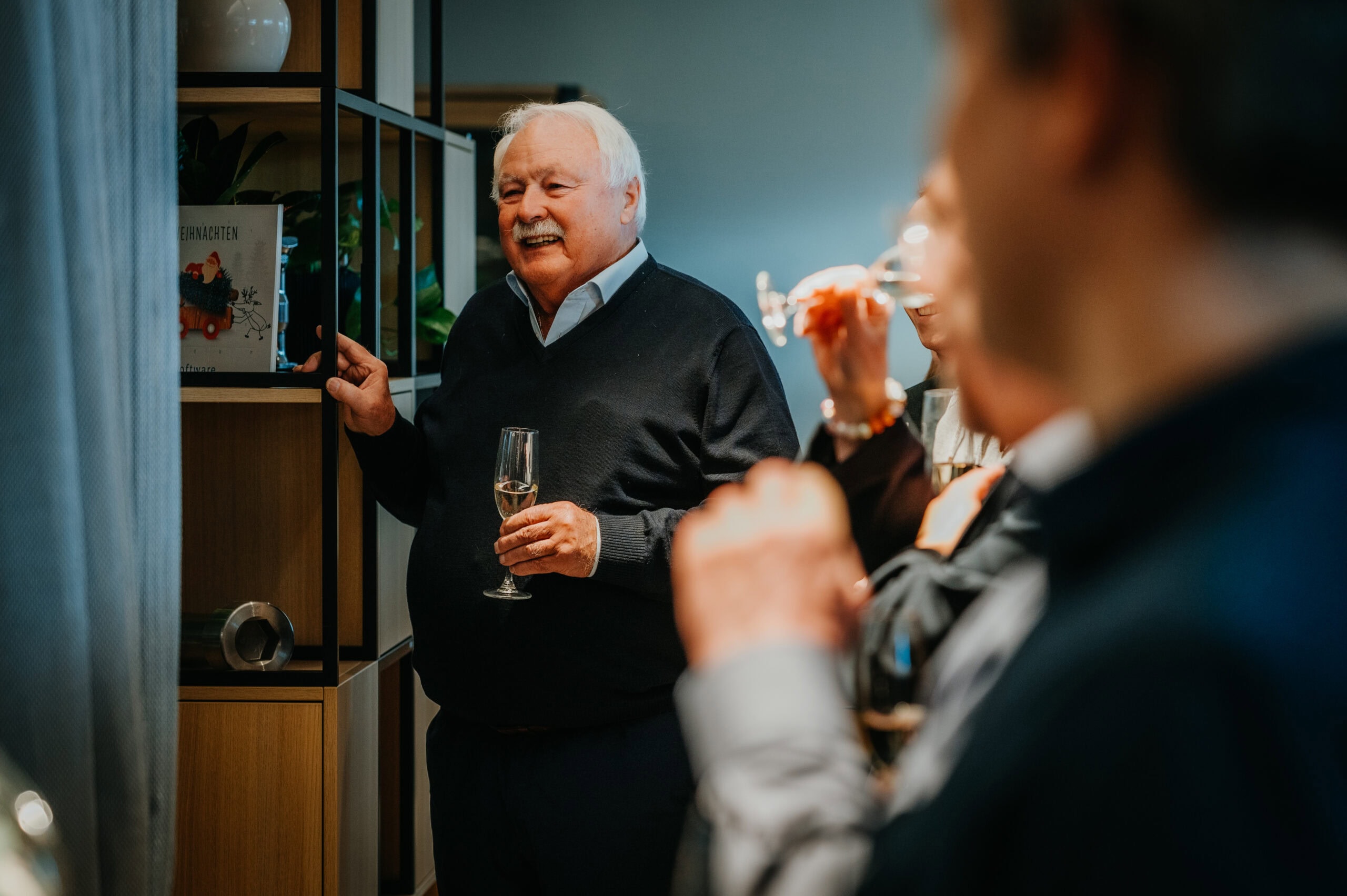 Älterer Mann bei Feier mit Champagner, umgeben von Gästen.
