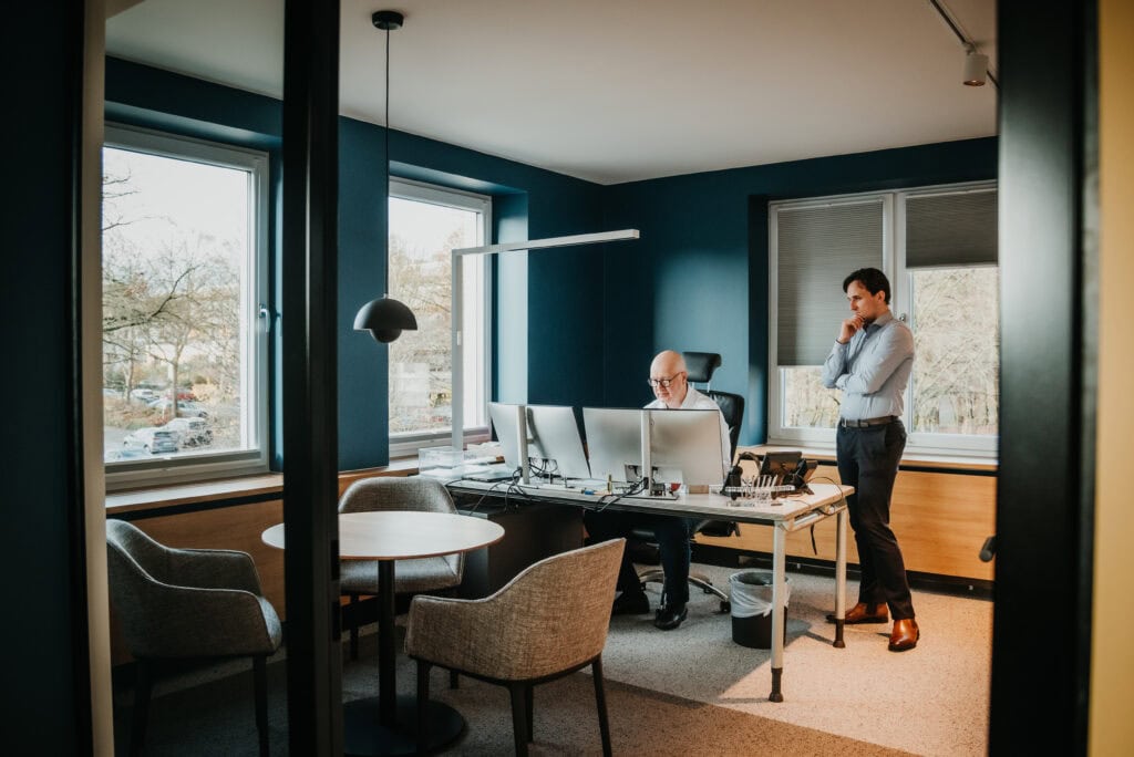 Zwei Männer arbeiten in einem modernen Büro mit großen Fenstern und Arbeitsplätzen.