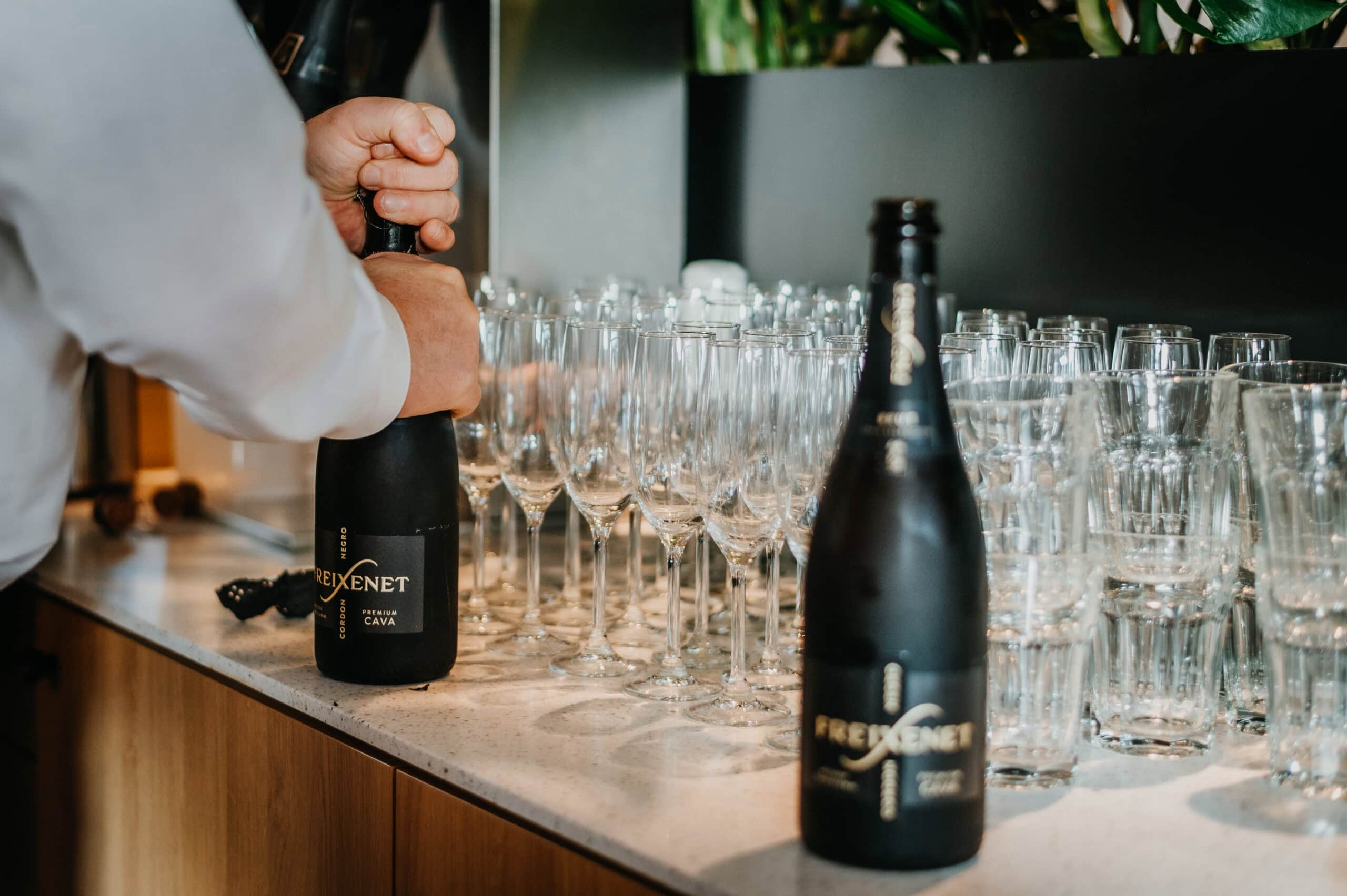 Person öffnet Champagnerflasche bei Event, Gläser bereit.