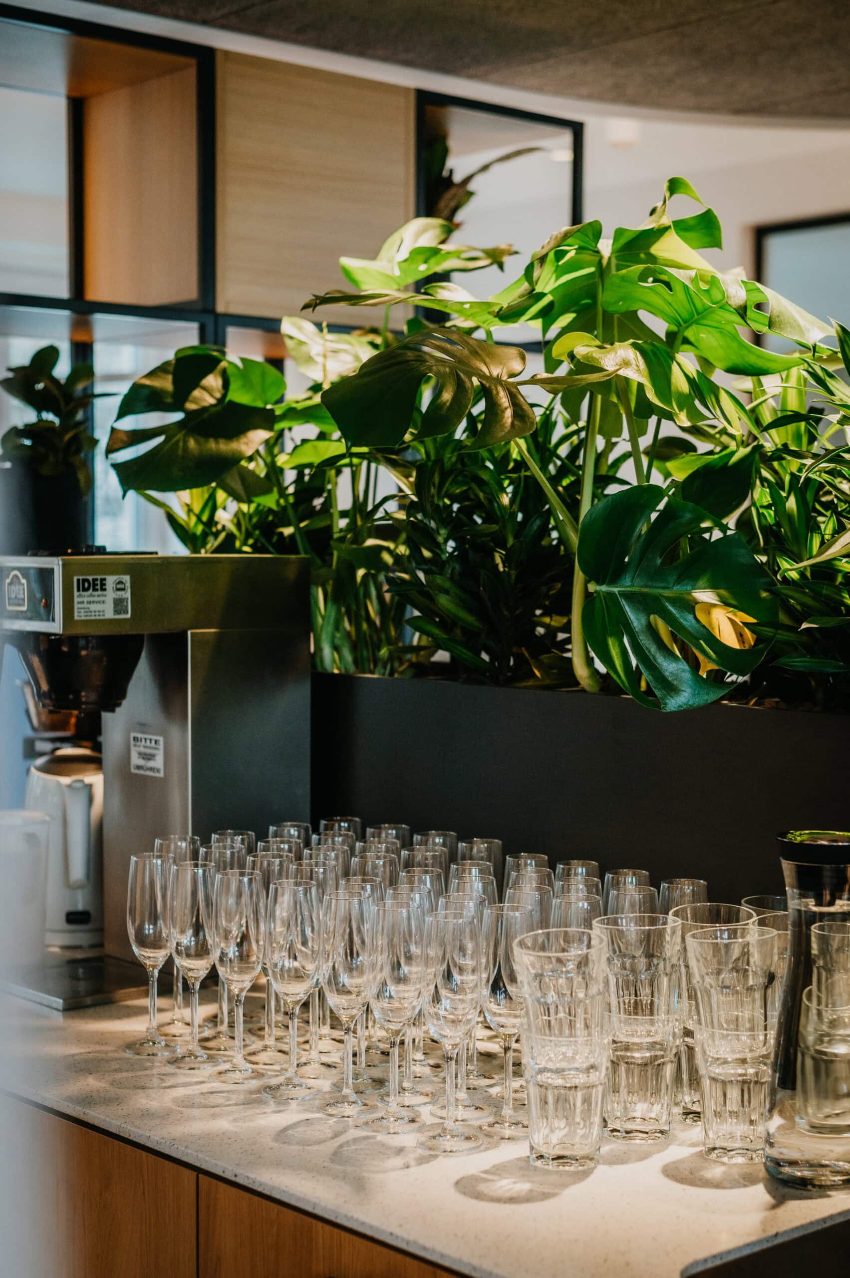 Blumenarrangement mit großen grünen Blättern und Glaswaren auf einer Theke.