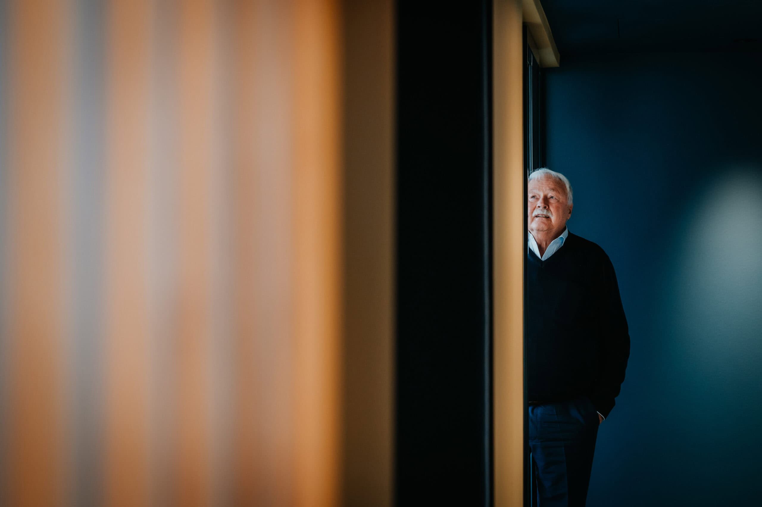 Älterer Mann schaut nachdenklich durch eine Türöffnung in einem modernen Gebäude.