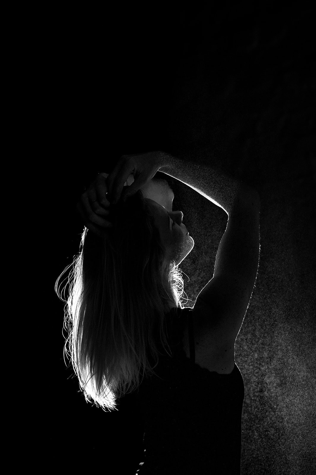 Silhouette einer Frau in dunklem Licht, die anmutig den Kopf neigt und die Hand im Haar hält.