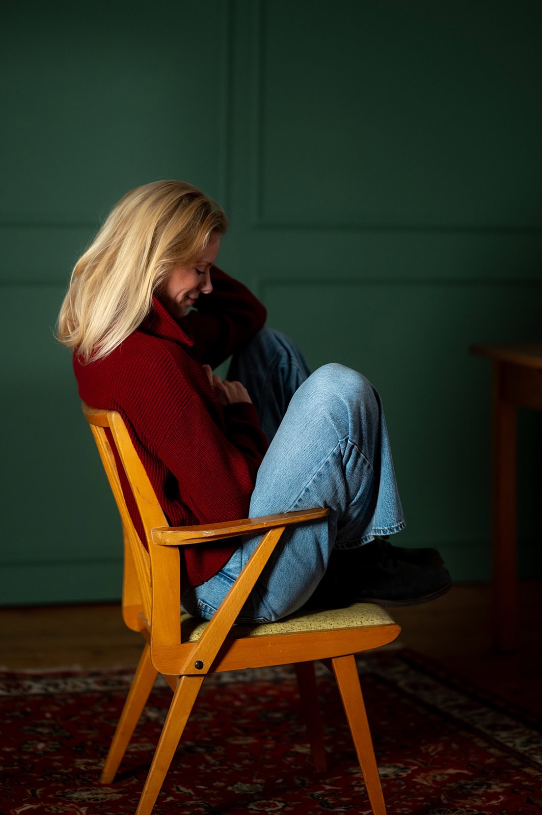 Frau sitzt entspannt auf einem Holzstuhl in einem grünen Raum.