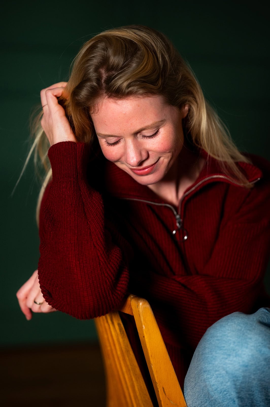 Junge Frau in rotem Pullover, nachdenklich und lächelnd, sitzend auf einem Stuhl.