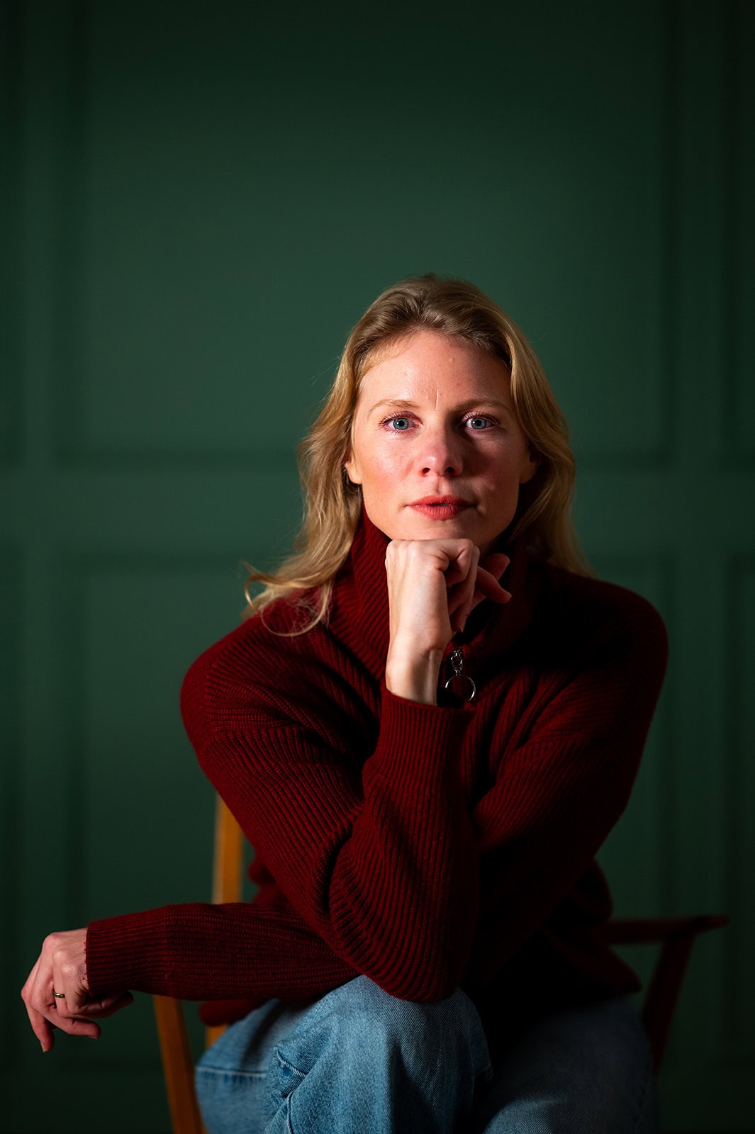 Nachdenkliche Frau in rotem Pullover vor grüner Wand, nachhaltiges Lifestyle-Konzept.