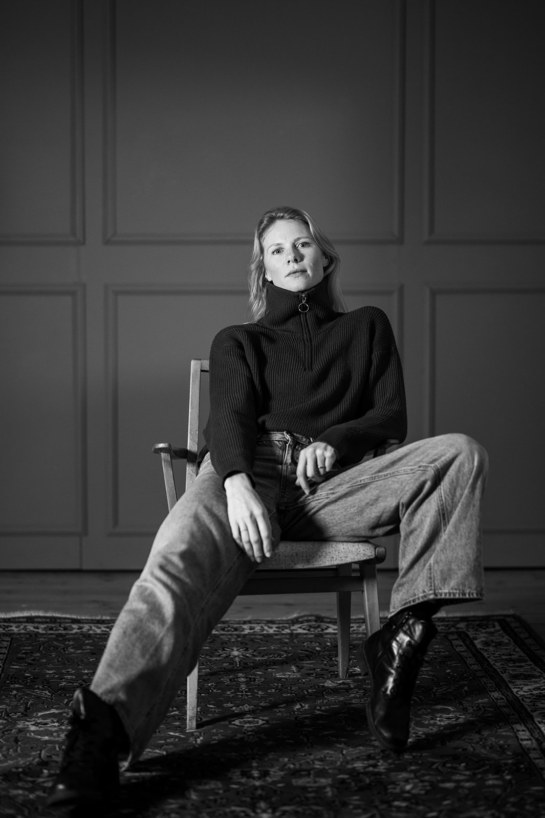 Frau im schwarzen Pullover sitzt entspannt auf einem Stuhl, schwarz-weiß Fotografie.