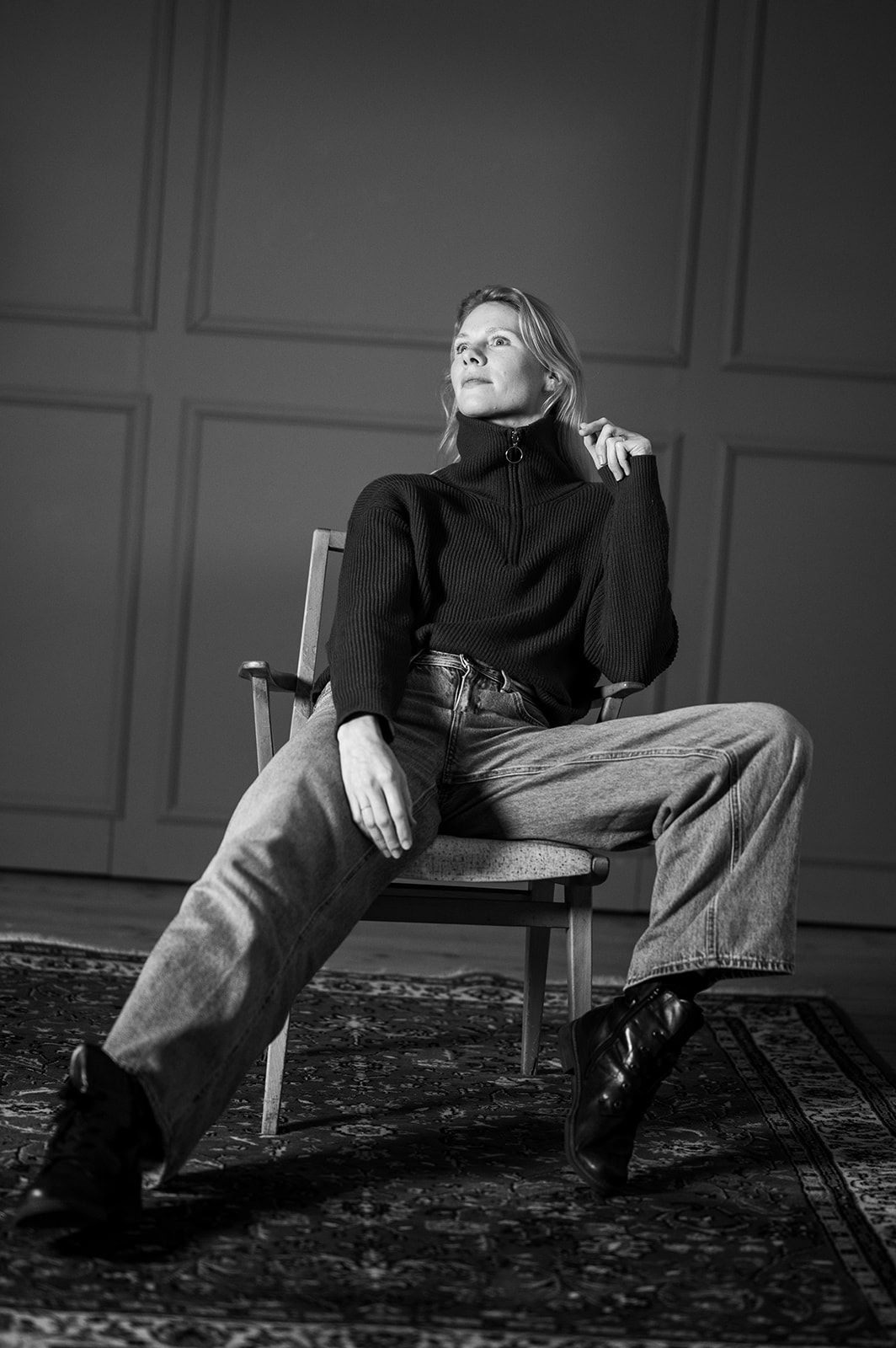 Frau in schwarzem Pullover und Jeans sitzt auf einem Stuhl, schwarz-weiß Bild.