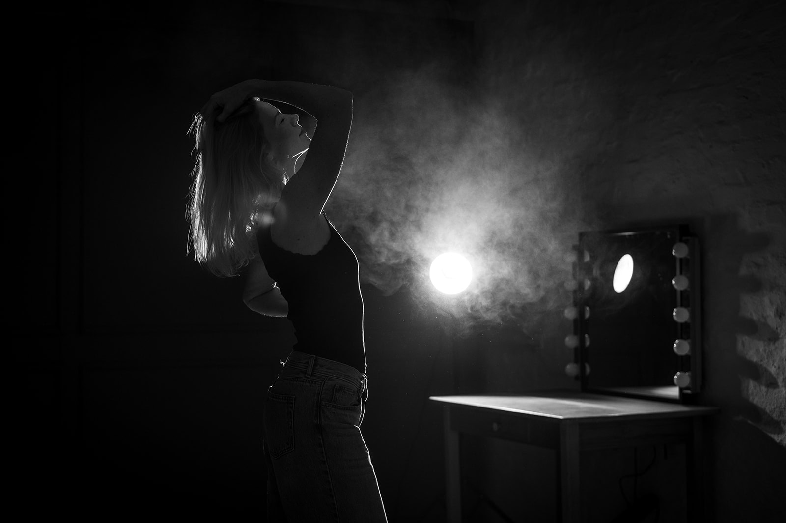 Frau posiert vor einem Spiegel mit Beleuchtung, künstlerisches Schwarz-Weiß-Foto.
